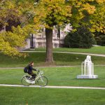 Student riding their bike past a public art installation