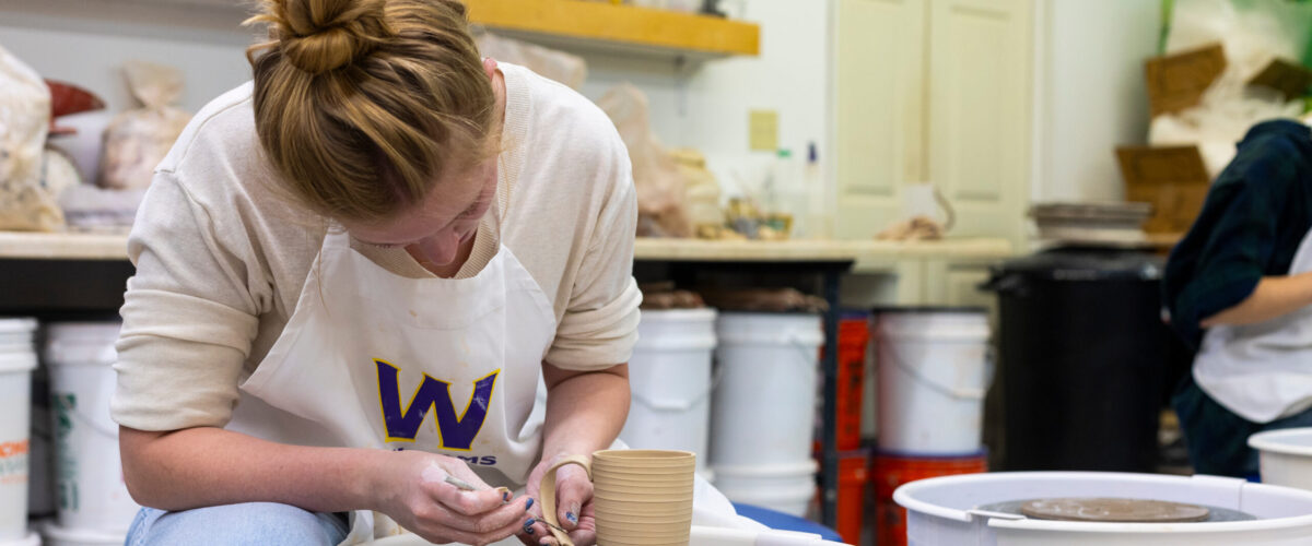A student sculpting a mug on a pottery wheel
