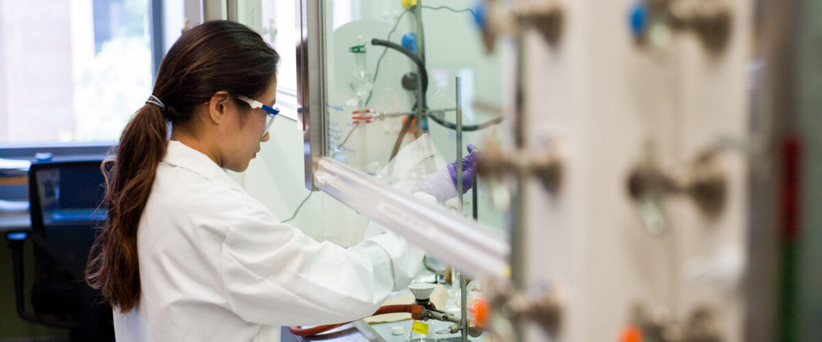 A student wearing a white lab coat working with equipment in a lab