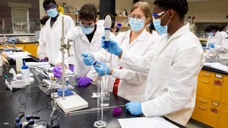 A professor trains students on scientific equipment in a lab