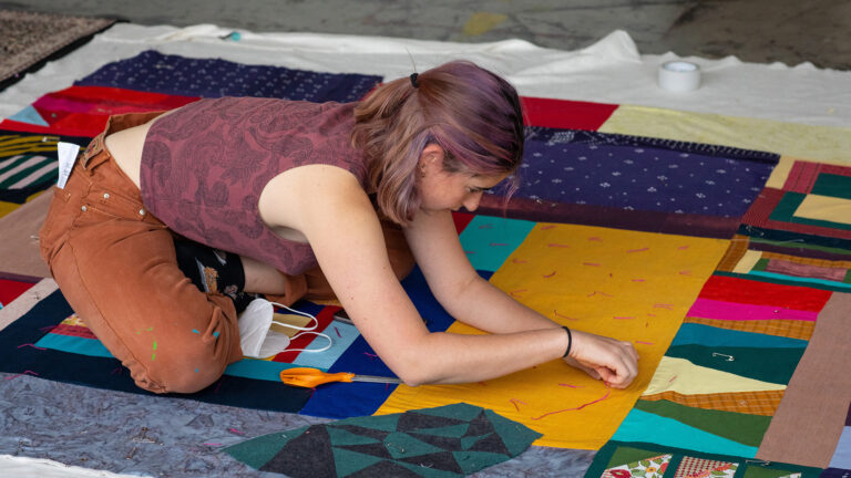 A student tacking fabric together while working on a textile project