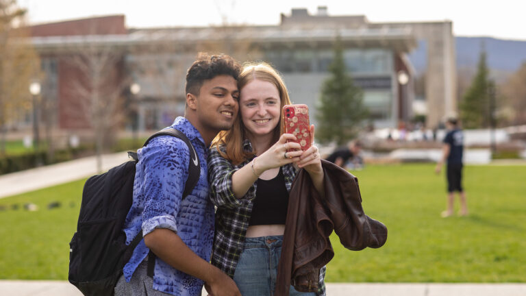 two students pose for a selfie against a backdrop of the main quad