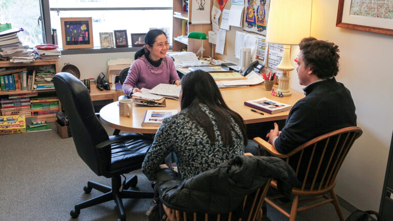 Two students sit across from a professor in her office holding a lively conversation