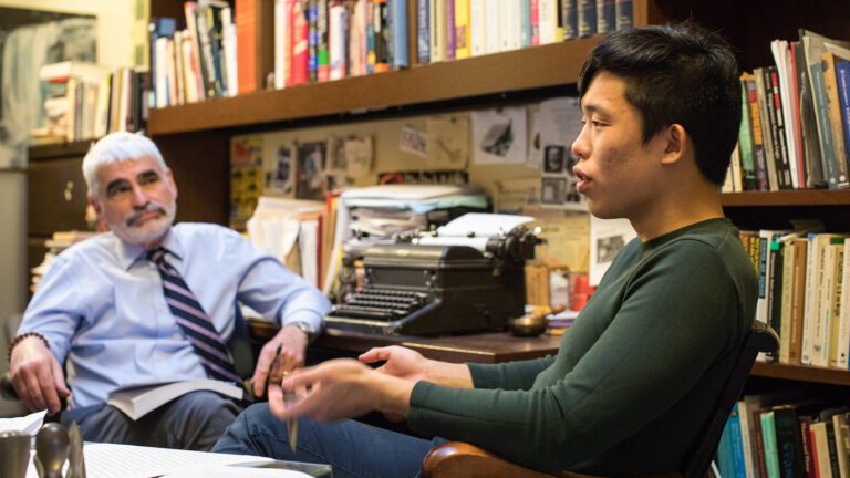 A student articulates a point while sitting across from a professor