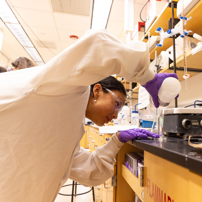 A student wearing a lab coat filling a beaker with a clear liquid