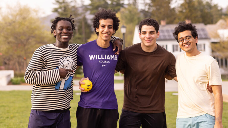 Four students with their arms around each others' shoulders smiling at the camera