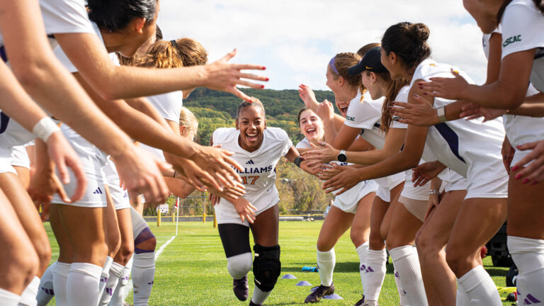 Photo of a group of soccer players high-fiving as a teammate runs by