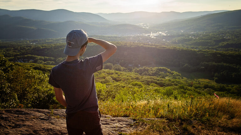 A student standing on a mountain overlooking North Adams and Williamstown