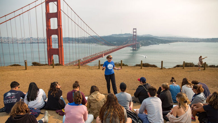 A group of students facing a presenter in front of the Golden Gate Bridge