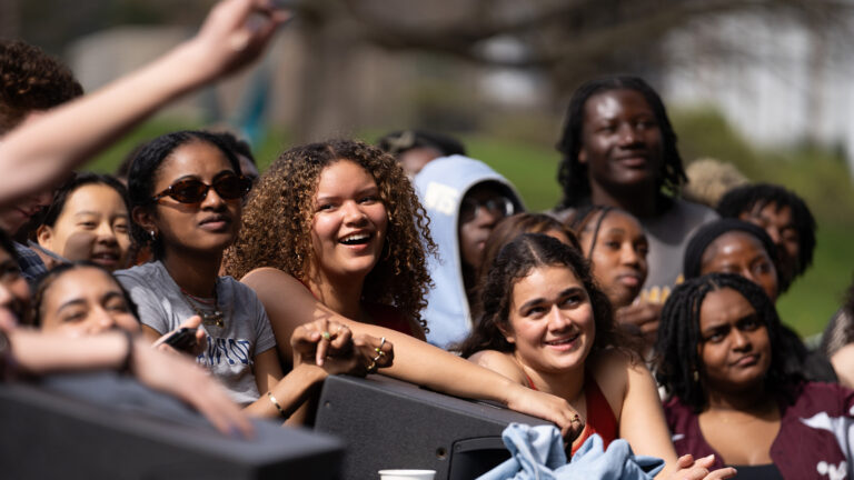 A group of students standing at the edge of a stage watching a performer