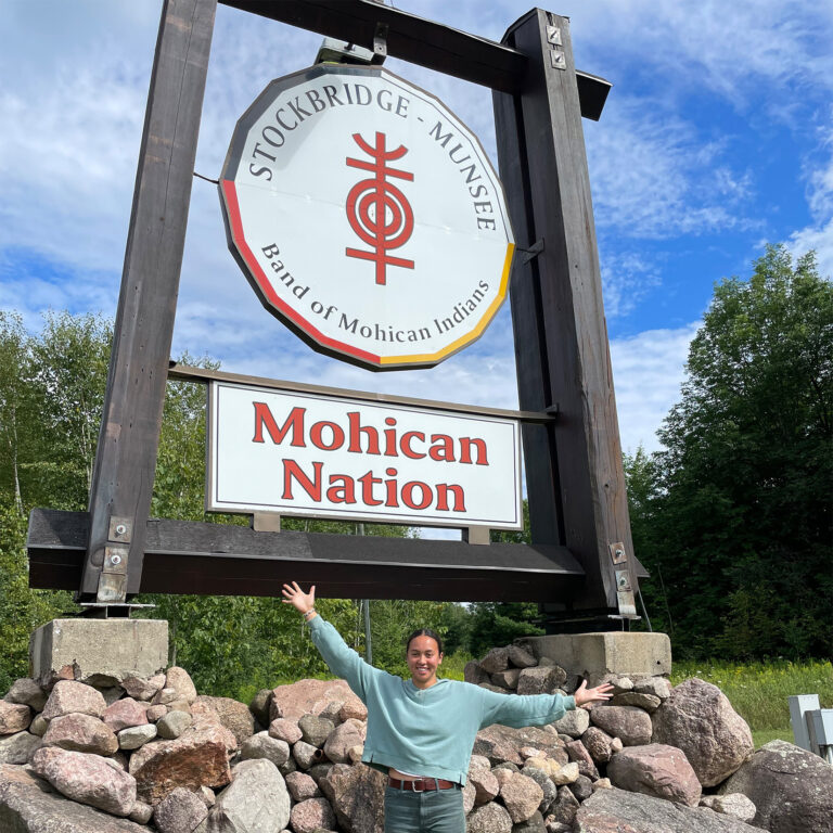 Student standing in front of a sign for the Stockbridge-Munsee Band of Mohican Indians land
