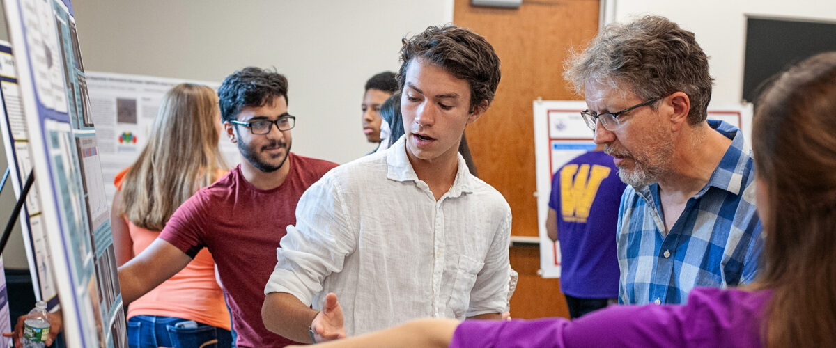 A student explains research displayed on a poster to a professor