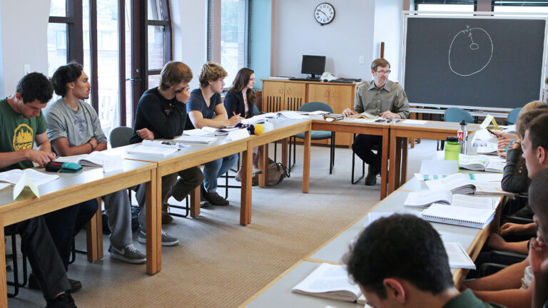 Professor Mark Reinhardt sitting at the head of the classroom and leading students