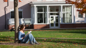 Student sitting against a tree while reading a book