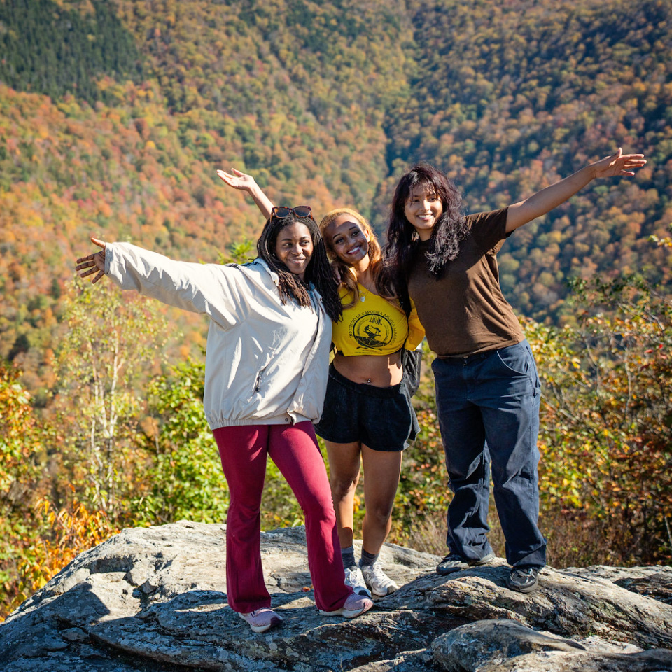 Three students at the top of a mountain pose for a photo agains a backdrop of the Berkshires