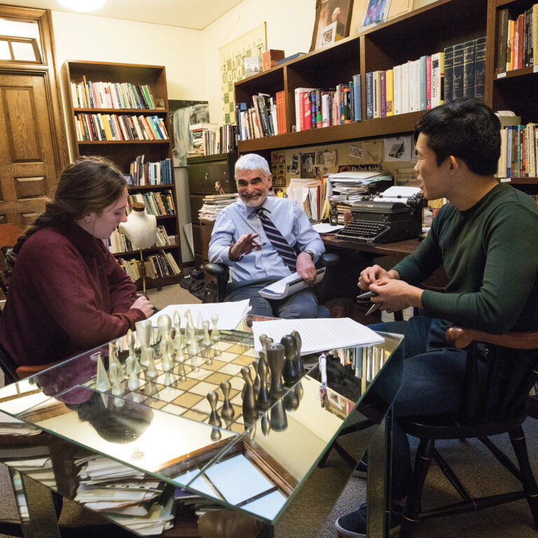two students sit in a professor's office having a lively conversation