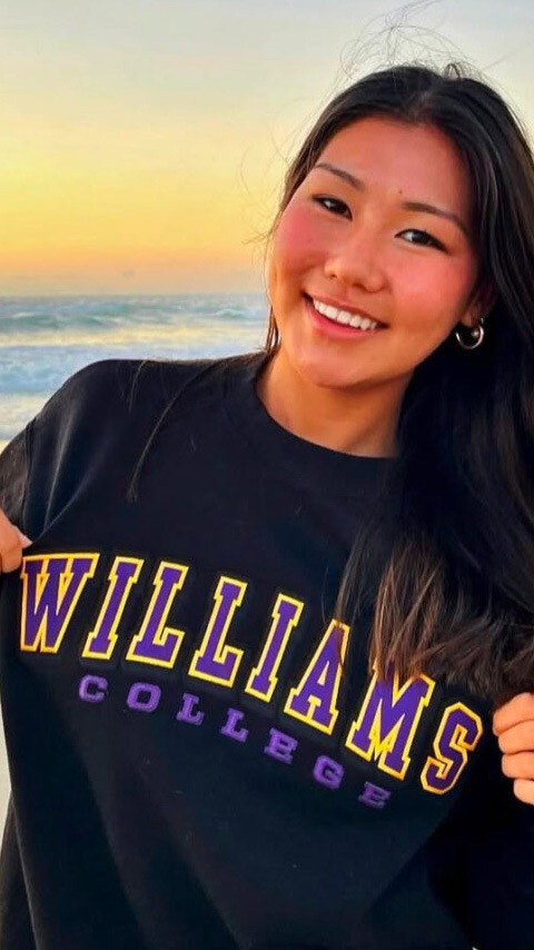 Jadyn Ganss shows off her Williams sweatshirt while standing on a beach at sunset