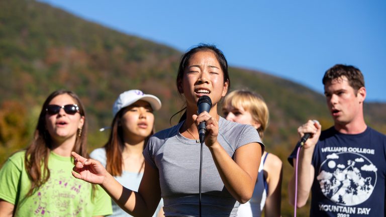 A group of students singing into microphones outside as part of a Mountain Day performance