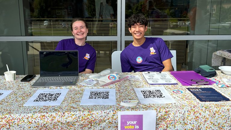 Two students sitting at a table encouraging other students to register to vote