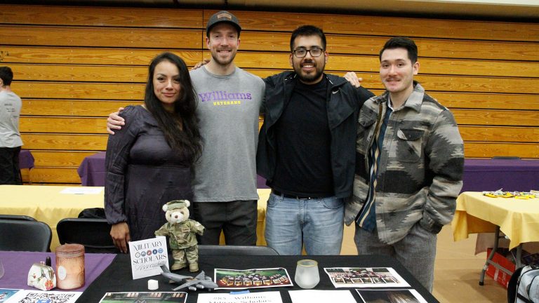 A group of students standing and posing behind a table for Military Scholars at a tabling event