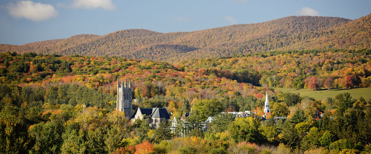 A view of campus from a distance with the trees on the mountains displaying fall colors