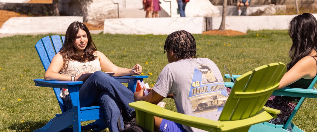 Three students sitting in high-backed chairs and studying on the Academic Quad
