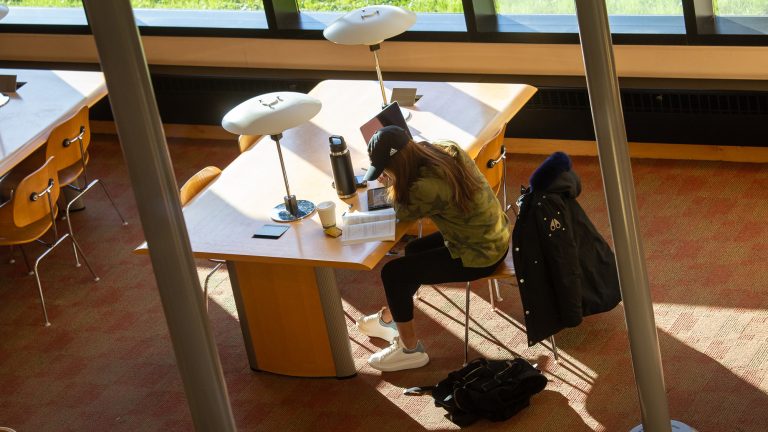 A student reading a book and taking notes on a tablet