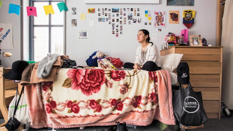A student sitting on a bed in a dorm room