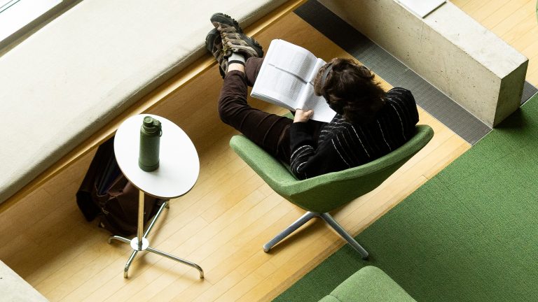 A student sitting in a chair while reading from a textbook in Sawyer Library