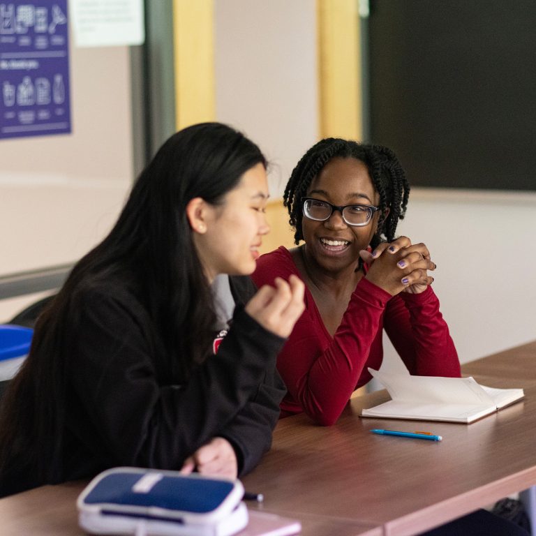 Two students discuss coursework in a classroom