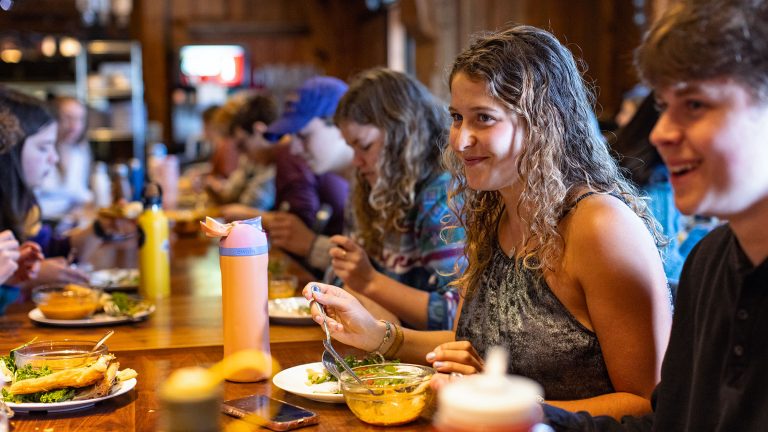 Students smile at a long table while eating lunch