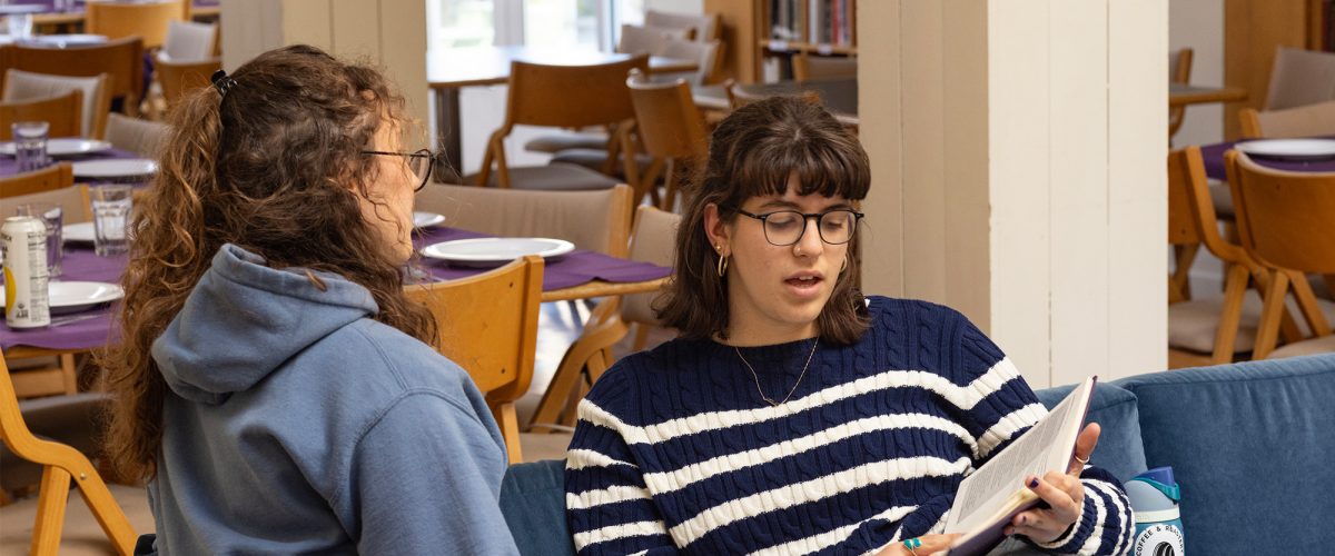 Two students sitting on a sofa and reading together from a book