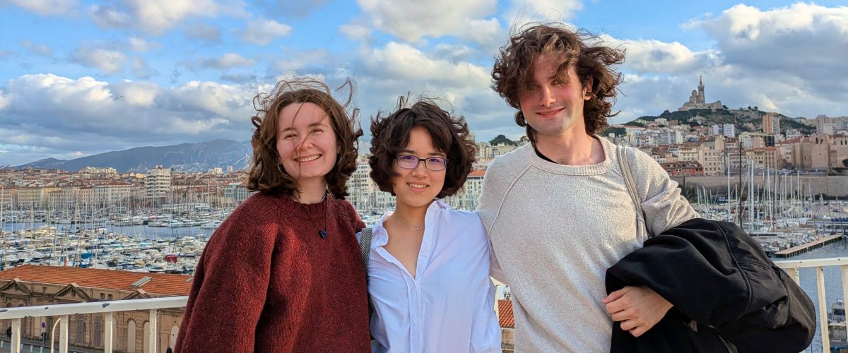 Three students posing for a photo with a European city in the background