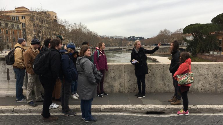 A group of Classics students listening to a speaker while standing on a bridge on a Study Abroad trip to Rome