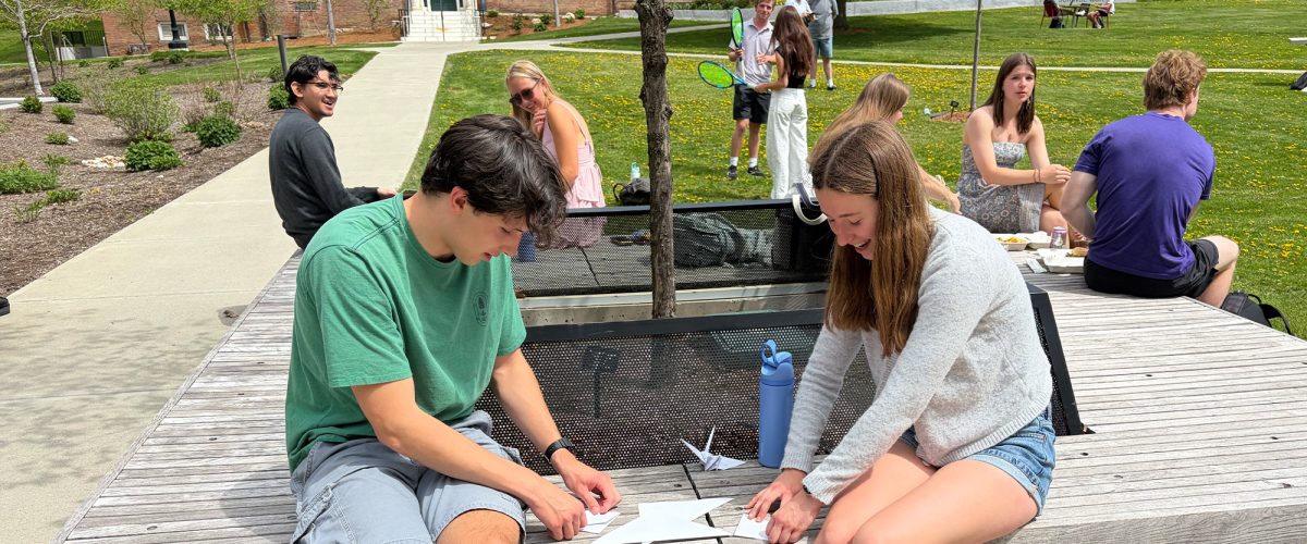 Students folding paper for origami on benches outdoors