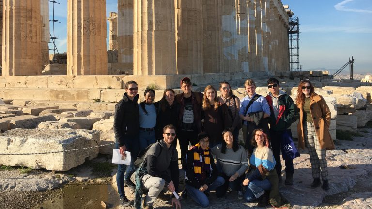 A group of Classics students posing for a photo in front of a historical ruin on a Study Abroad trip to Greece