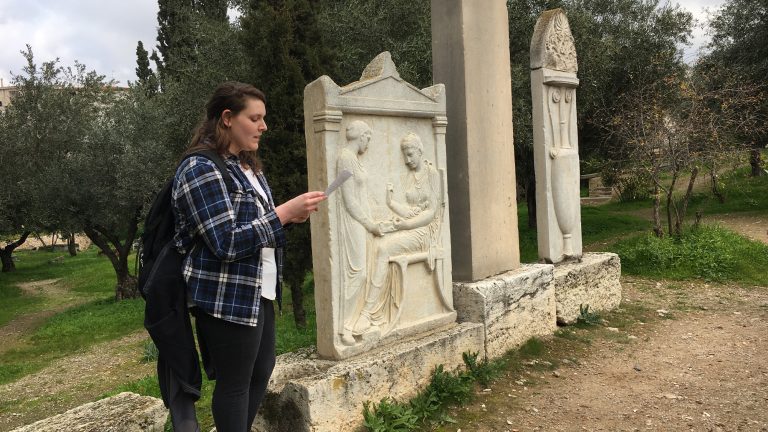 A Classics student on Study Abroad in Greece reading a text aloud next to artifacts outdoors