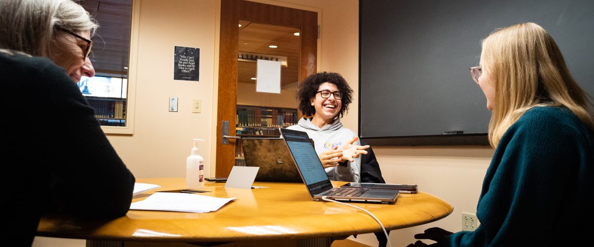 Two students and one professor talk around a table during a philosophy tutorial