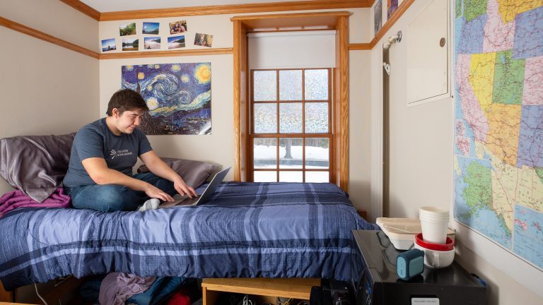 A student sitting on his dorm bed working on a laptop