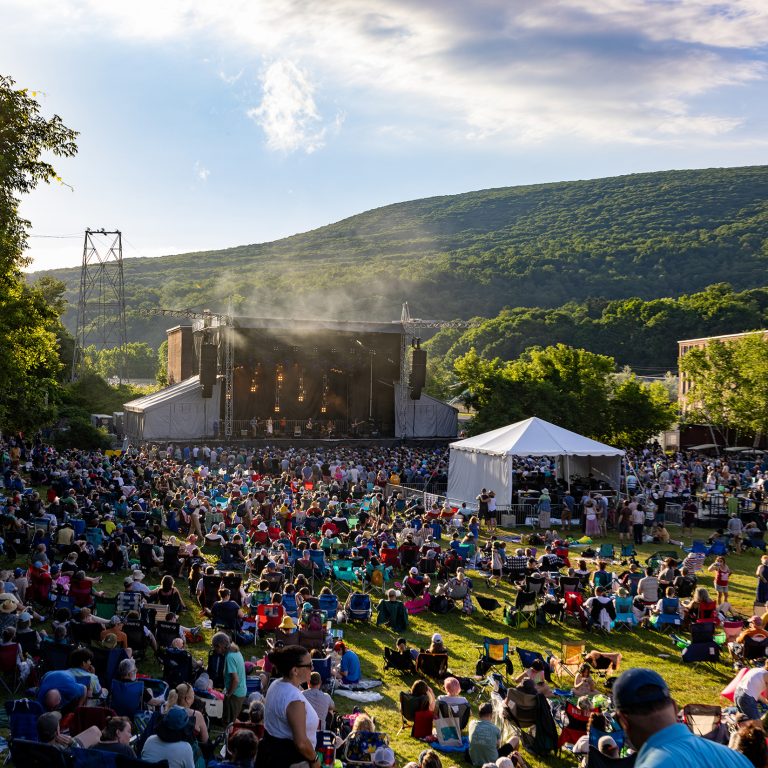 A crowd of people take in a concert amid the backdrop of the Berkshire Mountains
