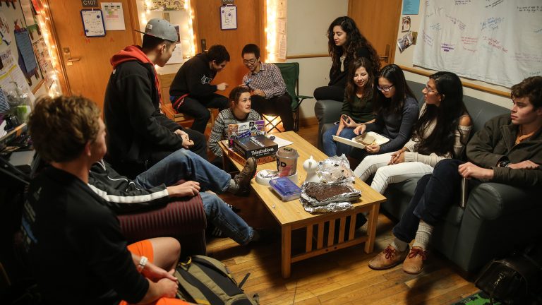 Students in a dorm common area talking and enjoying snacks