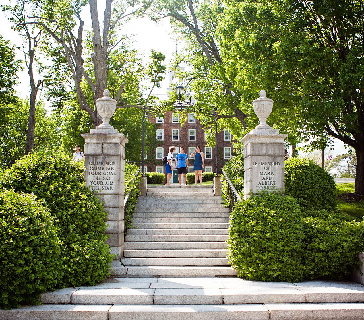 Students standing by hopkins gate with inscription 'climb high, climb far, your goal the sky, your aim the star'