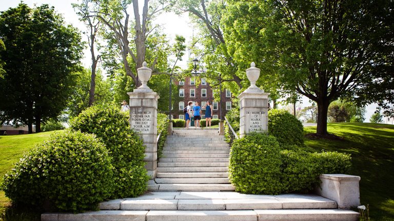 Students standing by hopkins gate with inscription 'climb high, climb far, your goal the sky, your aim the star'