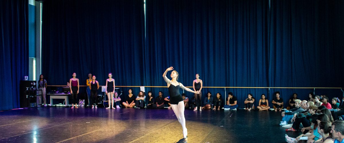 A student dancing solo surrounded by spectators sitting on the floor