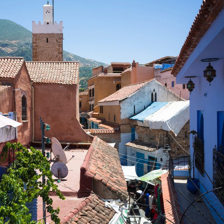 Image of historic rooftops in a residential setting in Morocco, with a glimpse into a street market below