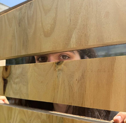 A student looking through a slat in the wall of the YouCube